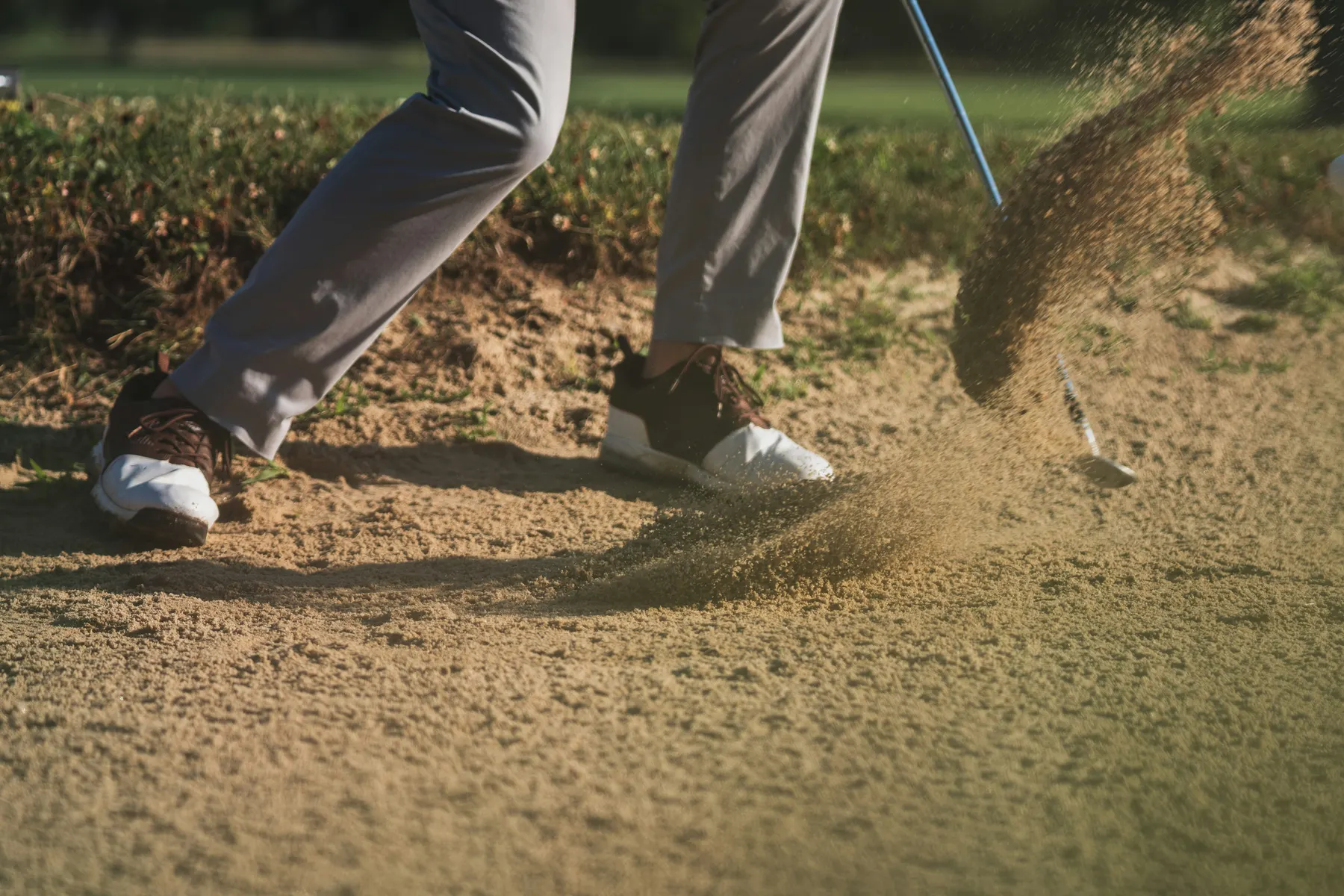 A golfer playing out of a bunker, sand spraying up from the club