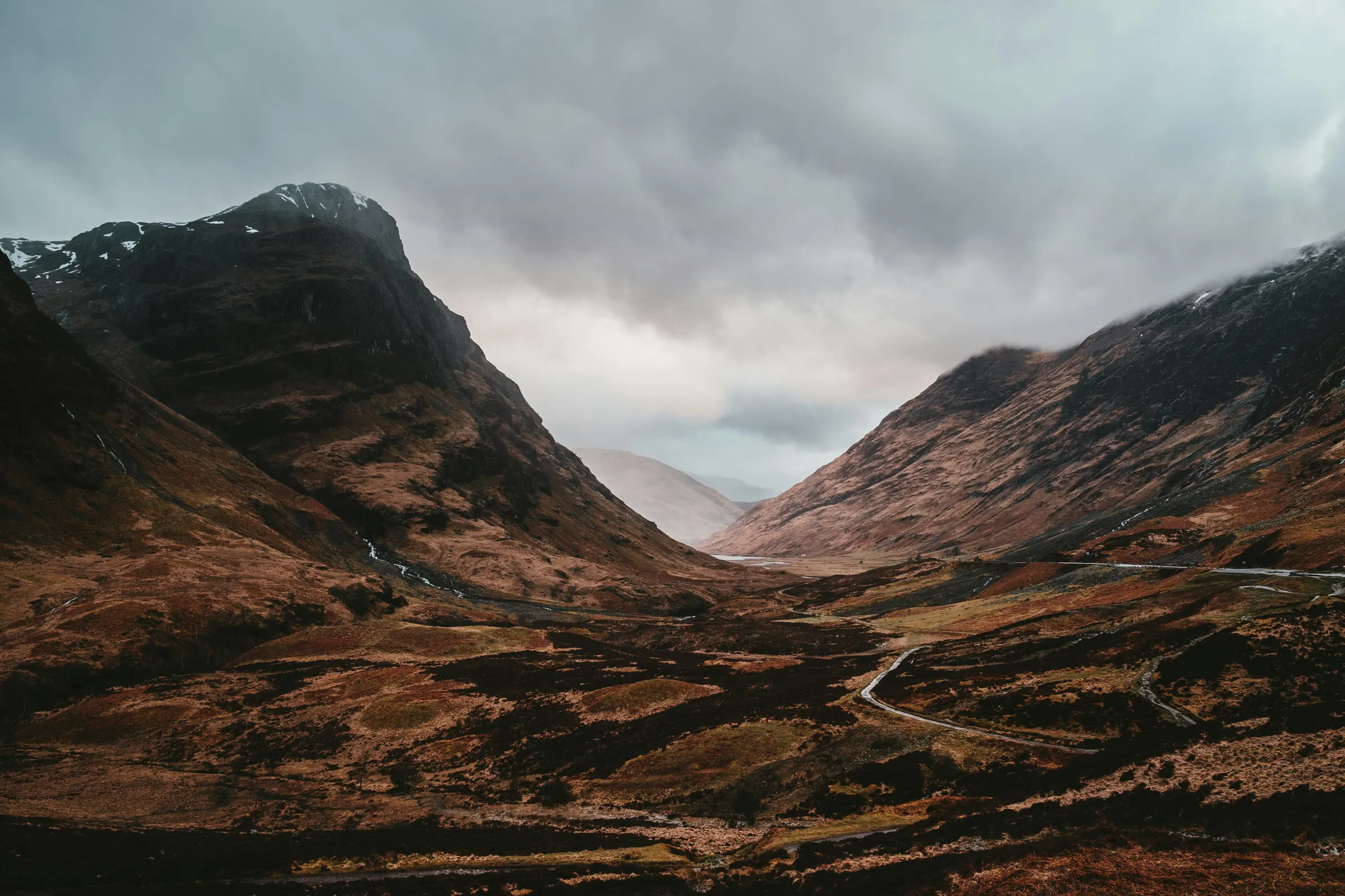 Cloud hanging low over the peaks of Glencoe, with a single road winding through the glen below