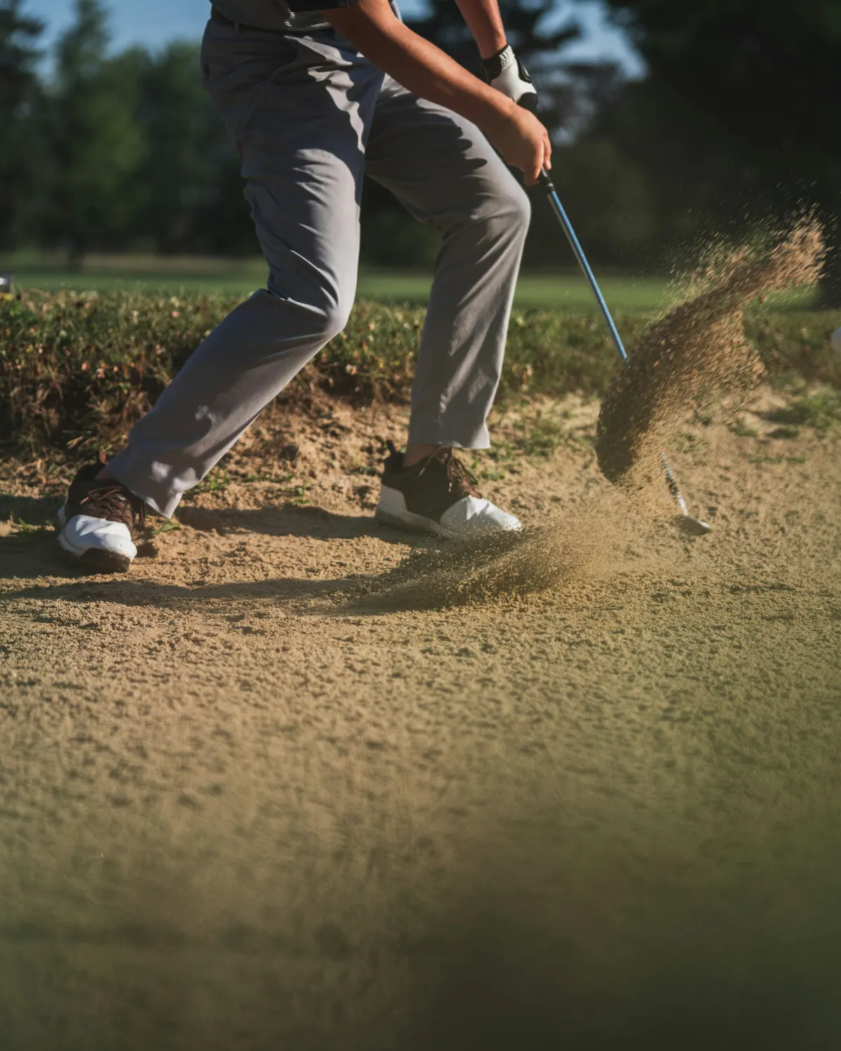 A golfer playing out of a bunker, sand spraying up from the club